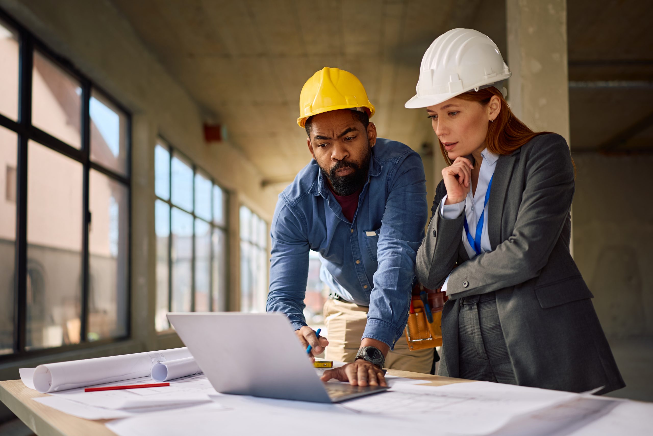 African American construction worker and female architect cooperating while using laptop at building site. Copy space.